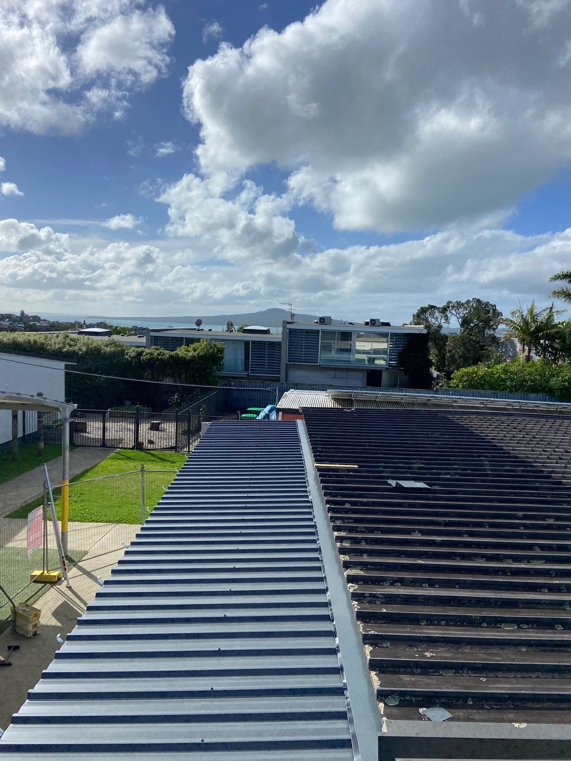 Blue and black rooftops under a cloudy blue sky. Buildings and green space in the background.