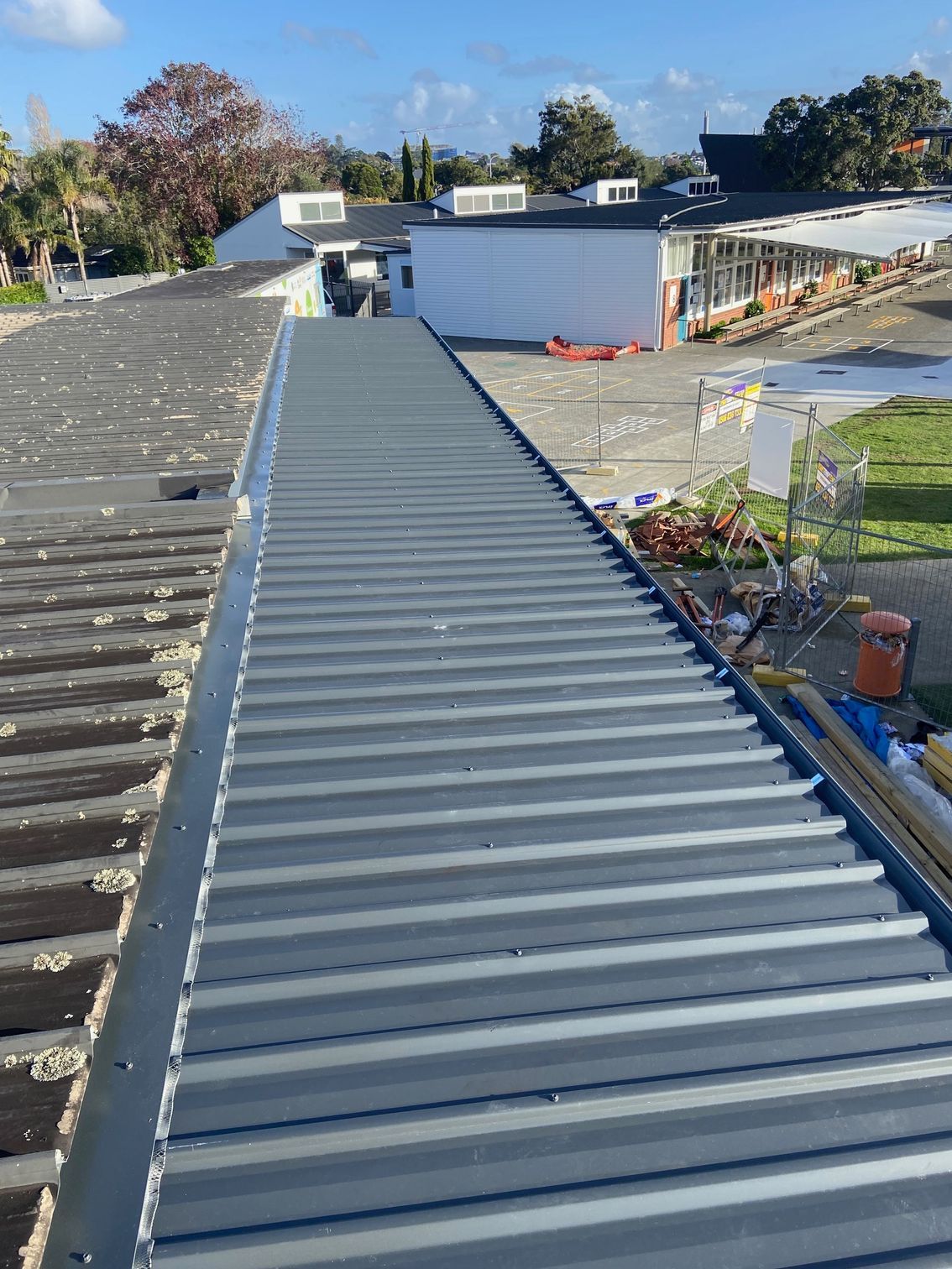 Newly installed gray metal roofing on a commercial building, with older roof visible on the side.