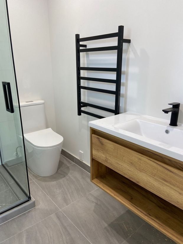 Bathroom with a wooden vanity, black towel rack, toilet, and shower stall.