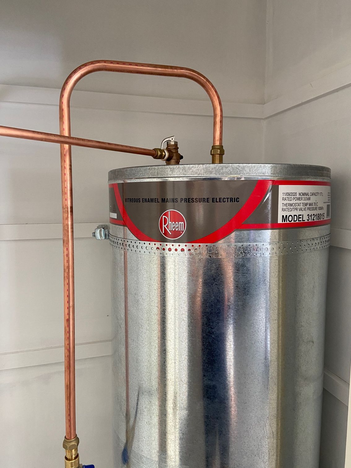 A copper-piped Rheem water heater in a white-walled enclosure.