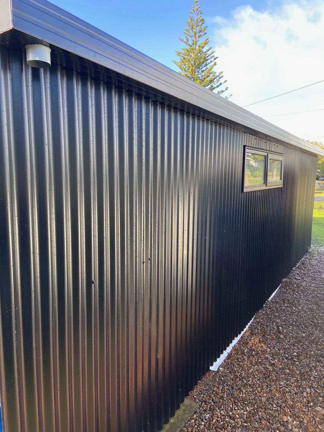 Black corrugated metal building with small windows, set against a blue sky.