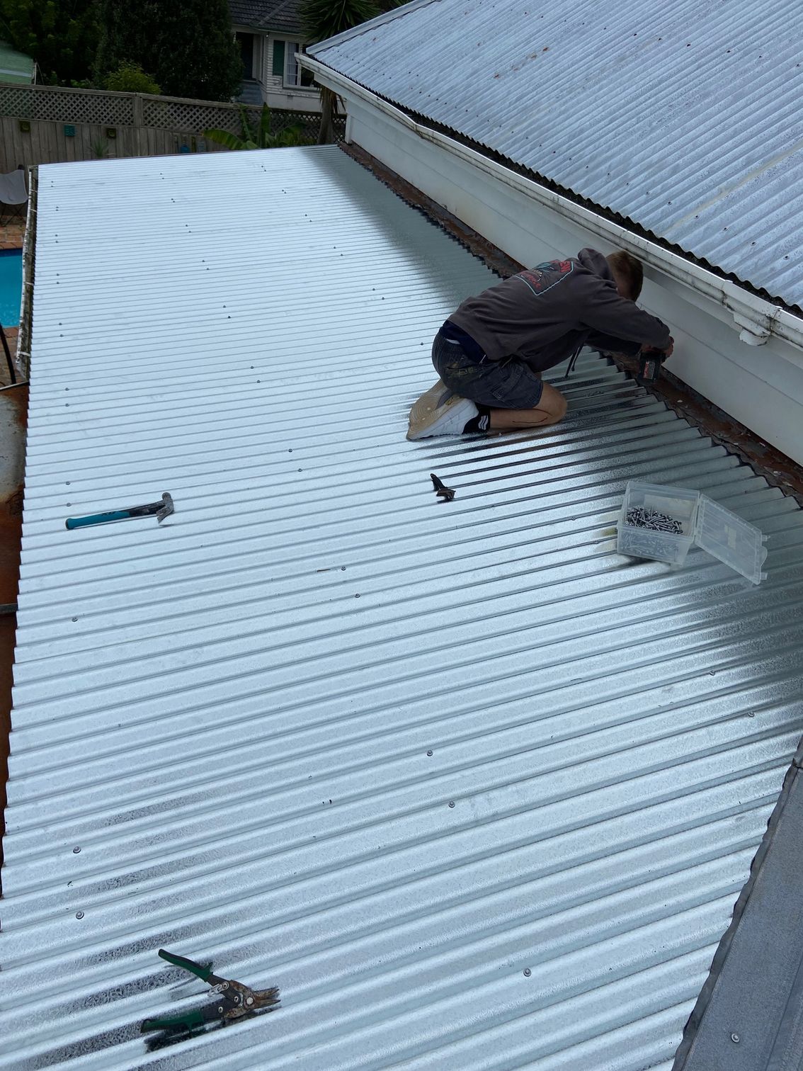 Person on a white corrugated metal roof, working near the edge of a building, tools visible.