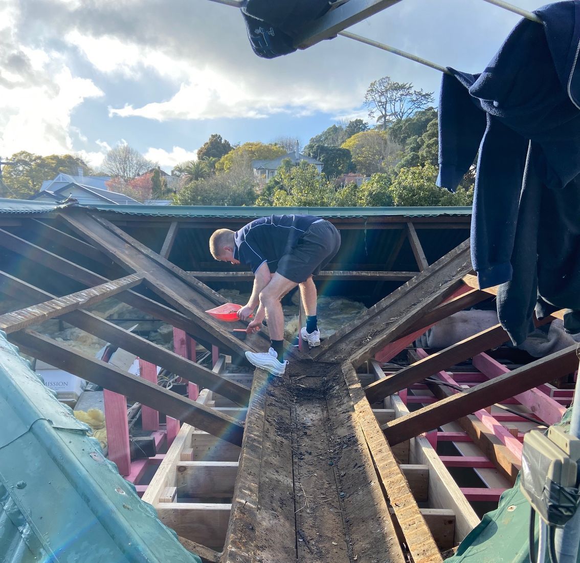 A man working on a roof. He is removing debris. The scene is outdoors on a sunny day.