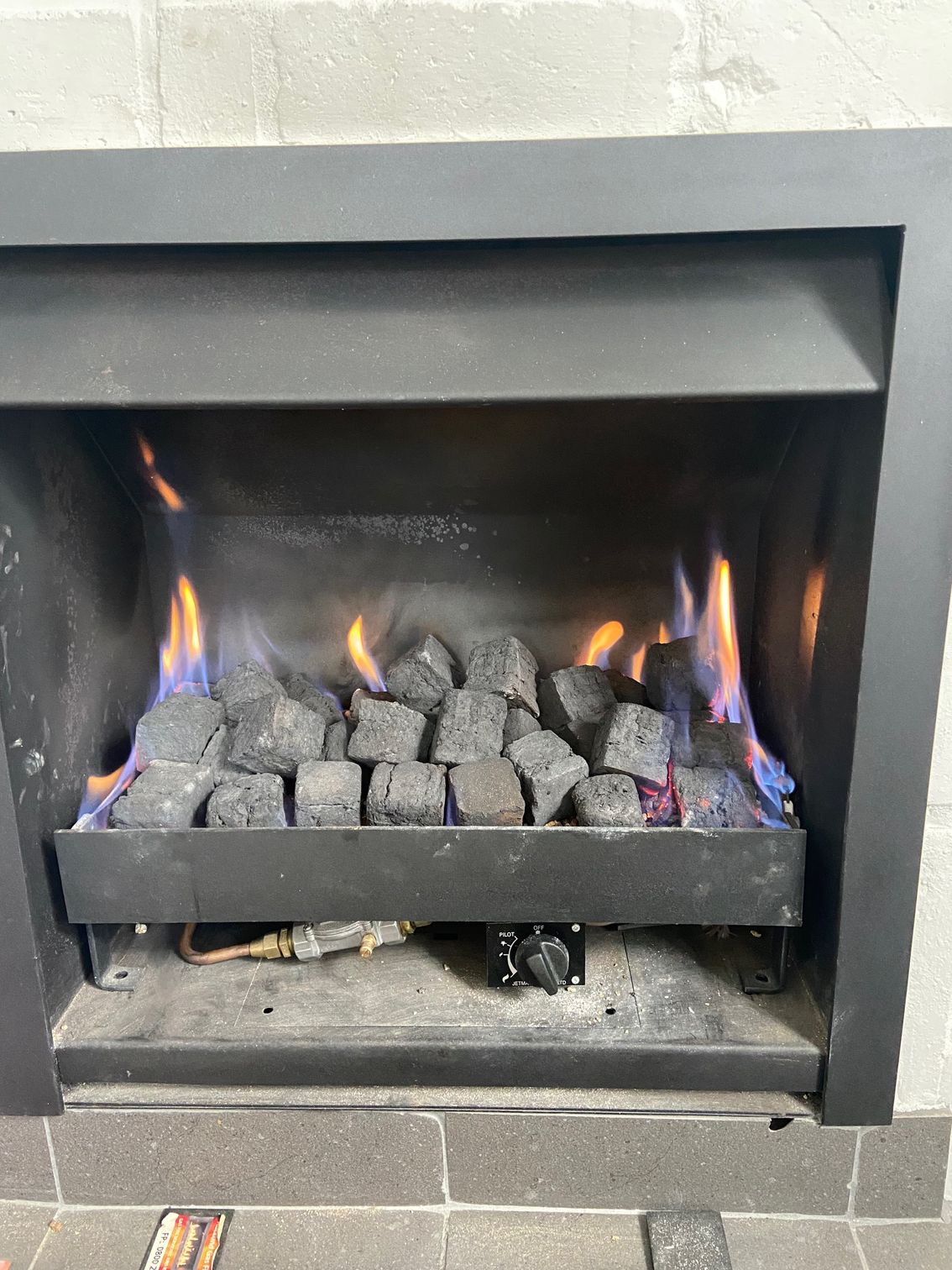 Fireplace with burning gas flames and charcoal-like logs inside a black metal frame.