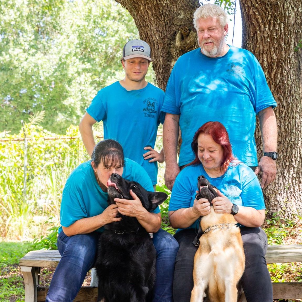 A group of people in blue shirts are posing for a picture with their dogs.