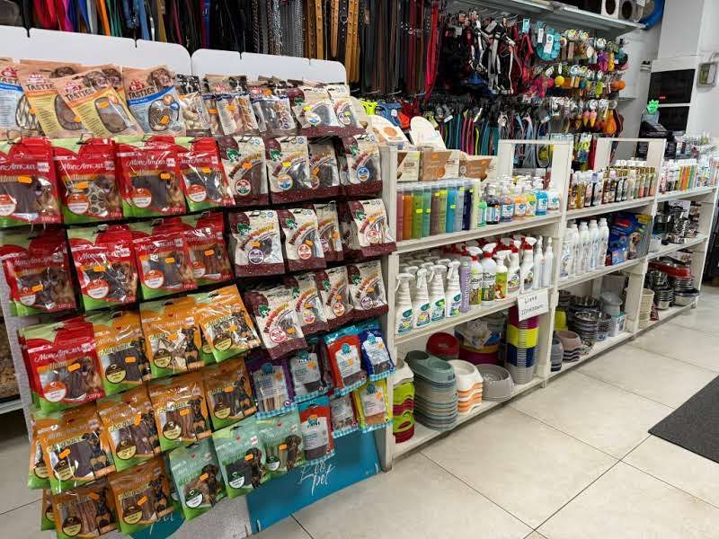 Scaffali di un negozio di articoli per animali domestici pieni di snack confezionati di vario tipo, spray per la toelettatura e diversi prodotti per la cura degli animali.