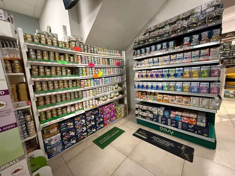 Corsie del negozio piene di scaffali di lattine e scatole di cibo per animali, con tappetini verdi davanti agli espositori.