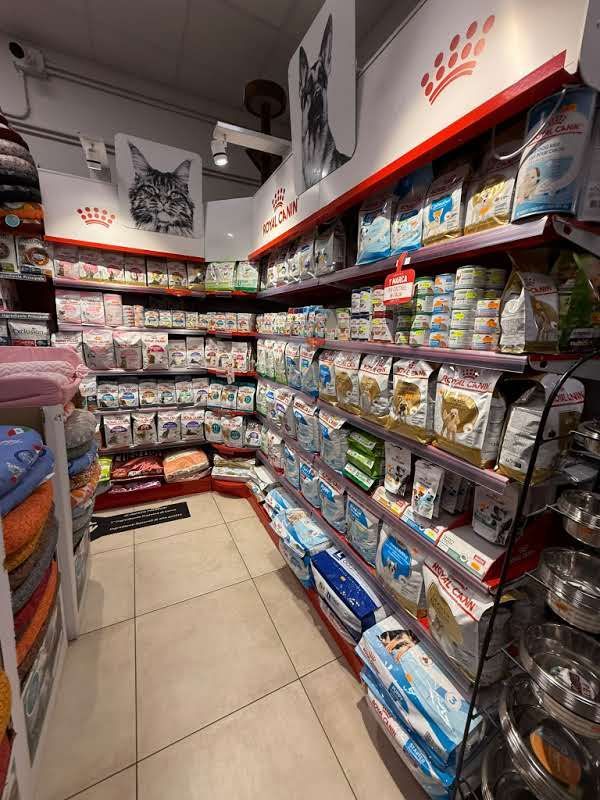 Il corridoio di un negozio di animali, con scaffali pieni di varie marche di cibo e accessori per animali, illuminati da luci intense.