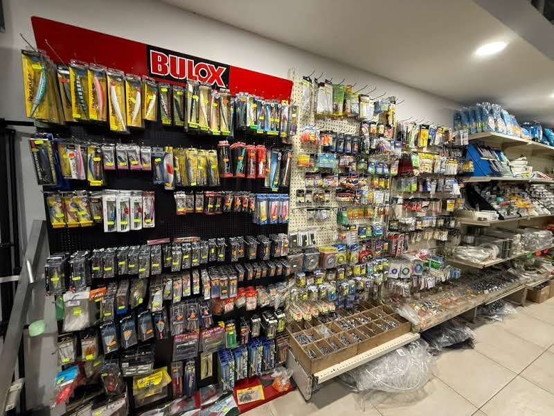 Vista interna di un negozio al dettaglio con scaffali e pannelli forati densamente riforniti di vari articoli e accessori da pesca.