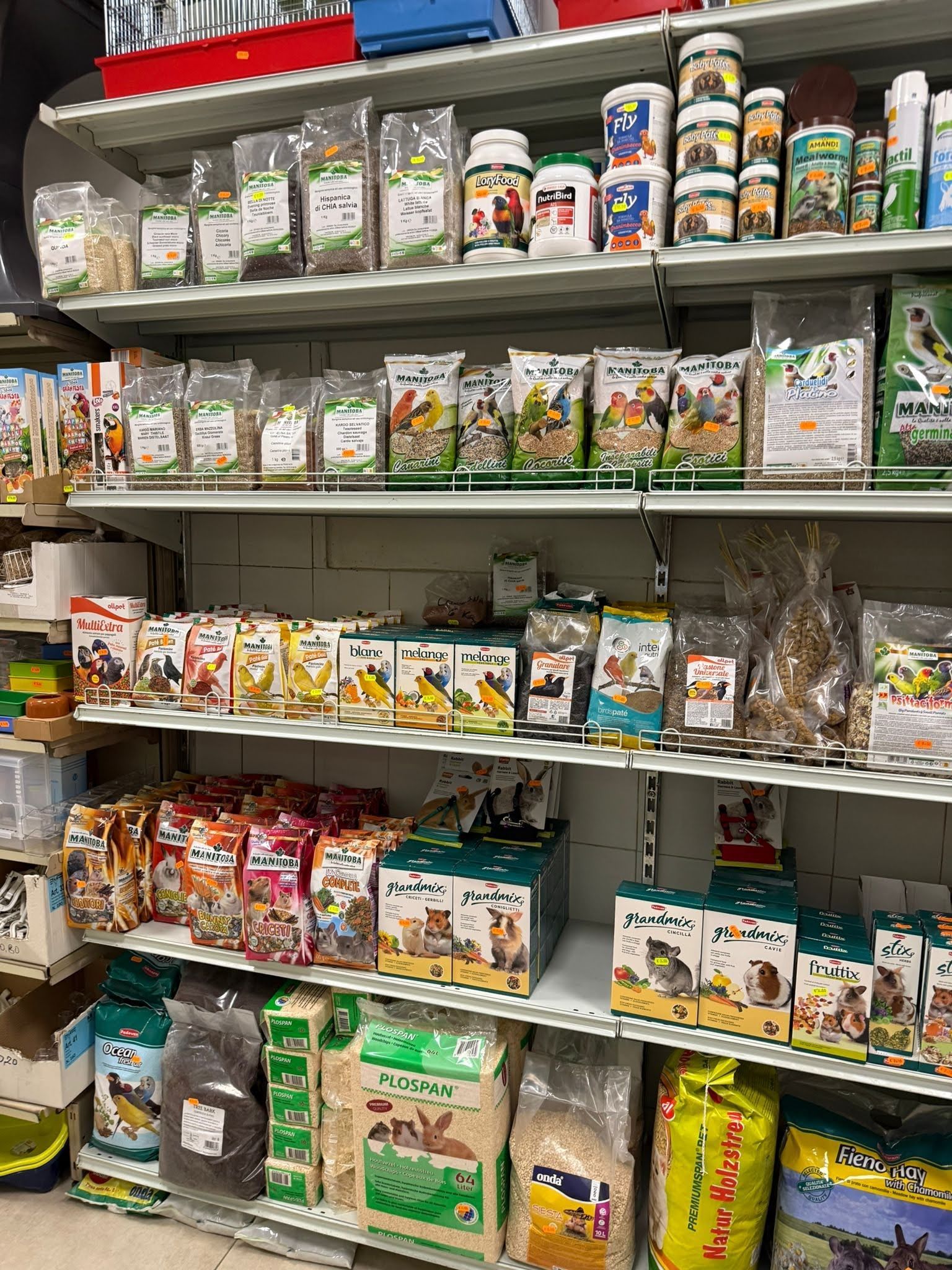 In un negozio, gli scaffali sono pieni di sacchetti, contenitori e accessori per alimenti per animali domestici di vario tipo.