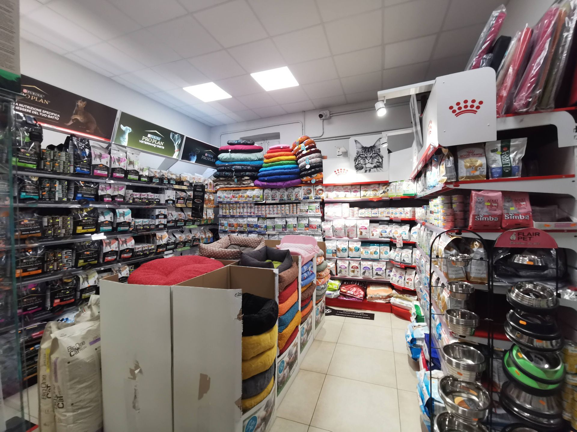 All'interno di un negozio di animali ben illuminato, con scaffali pieni di cibo per animali, cucce colorate e ciotole di metallo in vendita.