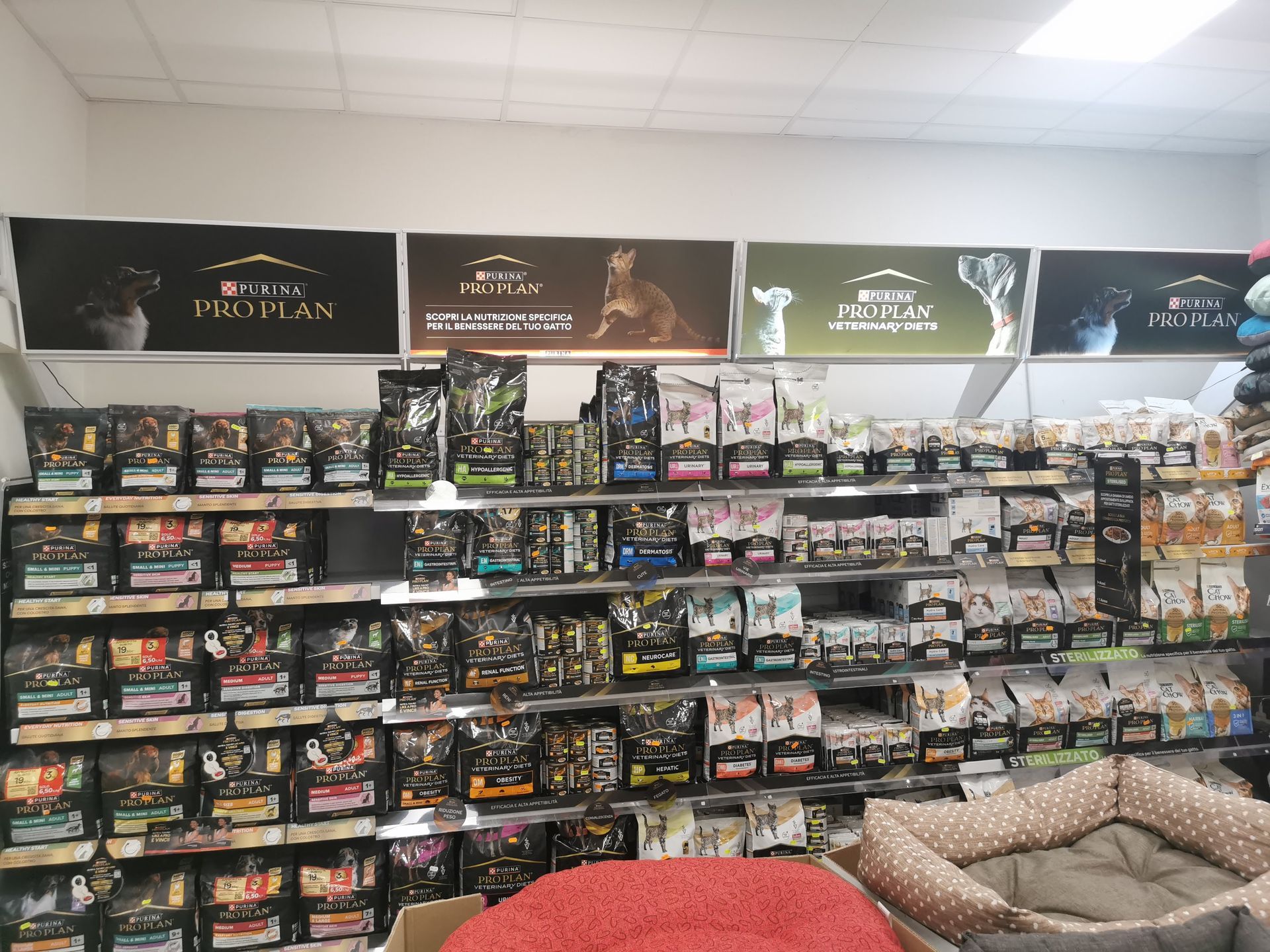 In un negozio al dettaglio, sugli scaffali sono esposti vari sacchi di cibo per animali Purina Pro Plan, con delle cucce in primo piano.
