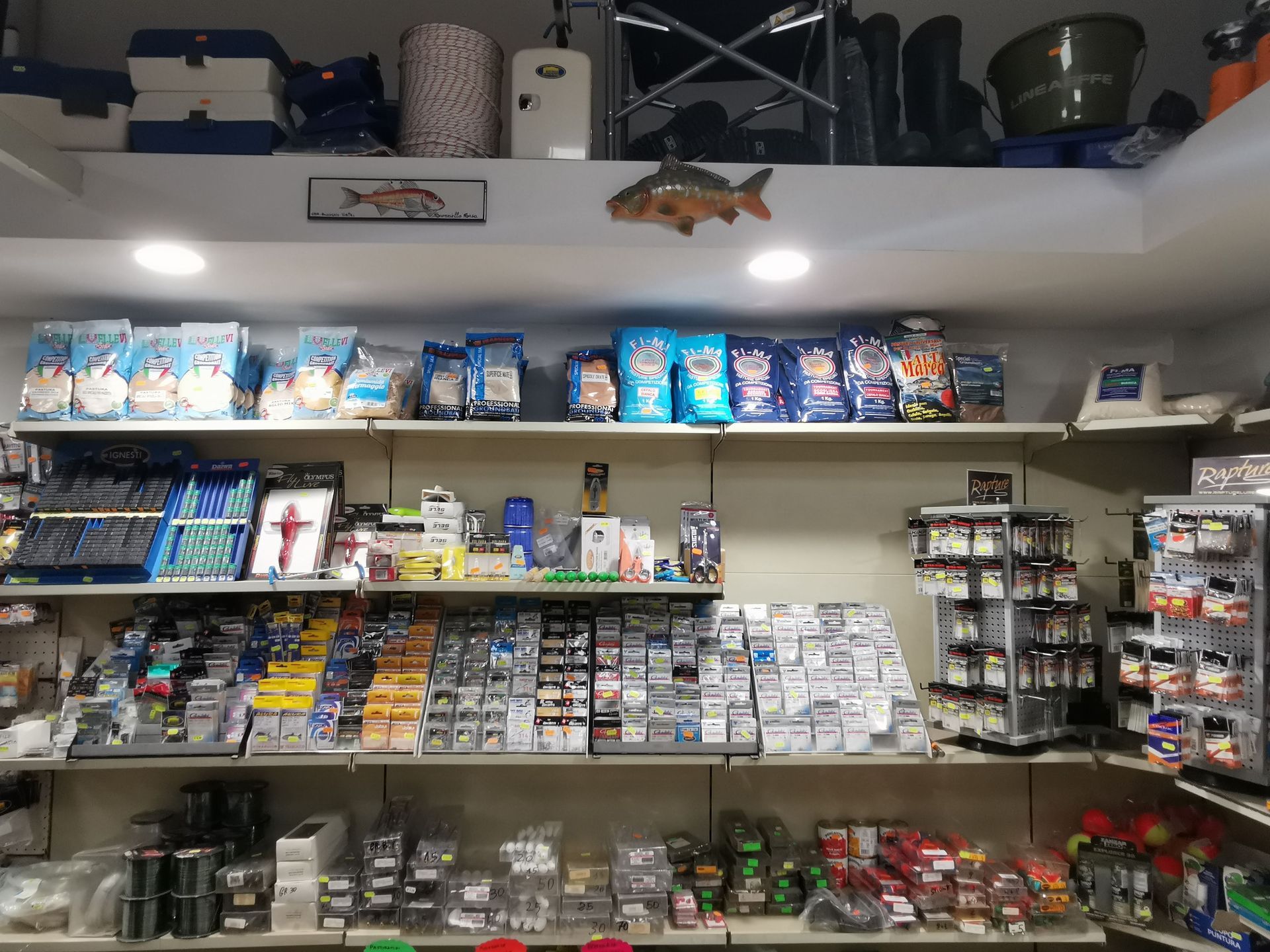Scaffali di un negozio di articoli da pesca pieni di esche, ami, scatole per attrezzatura e altri articoli correlati alla pesca.