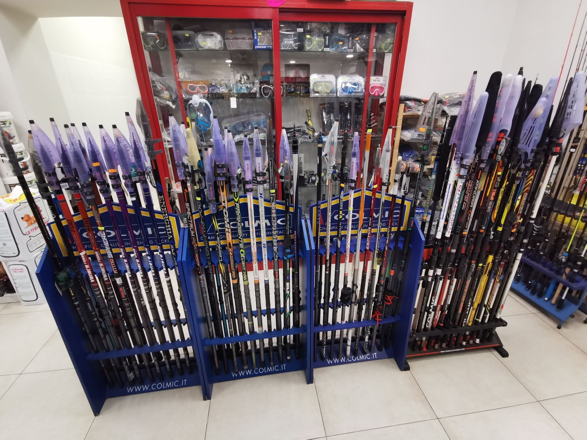 Un espositore per negozi che mostra numerose canne da pesca su supporti blu, con una vetrina rossa sullo sfondo.