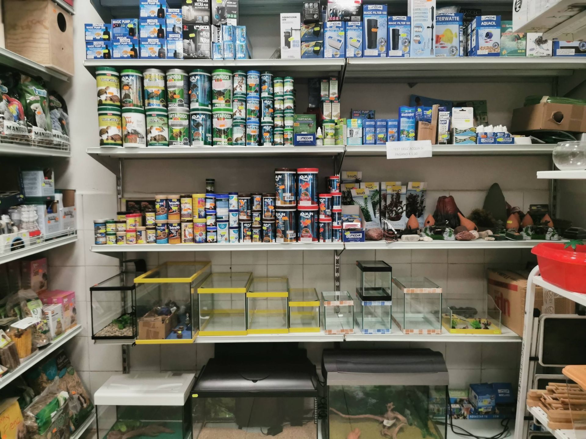 Scaffali riforniti di articoli per acquari, tra cui lattine di cibo per animali, piccole vasche di vetro e apparecchiature per la filtrazione dell'acqua.