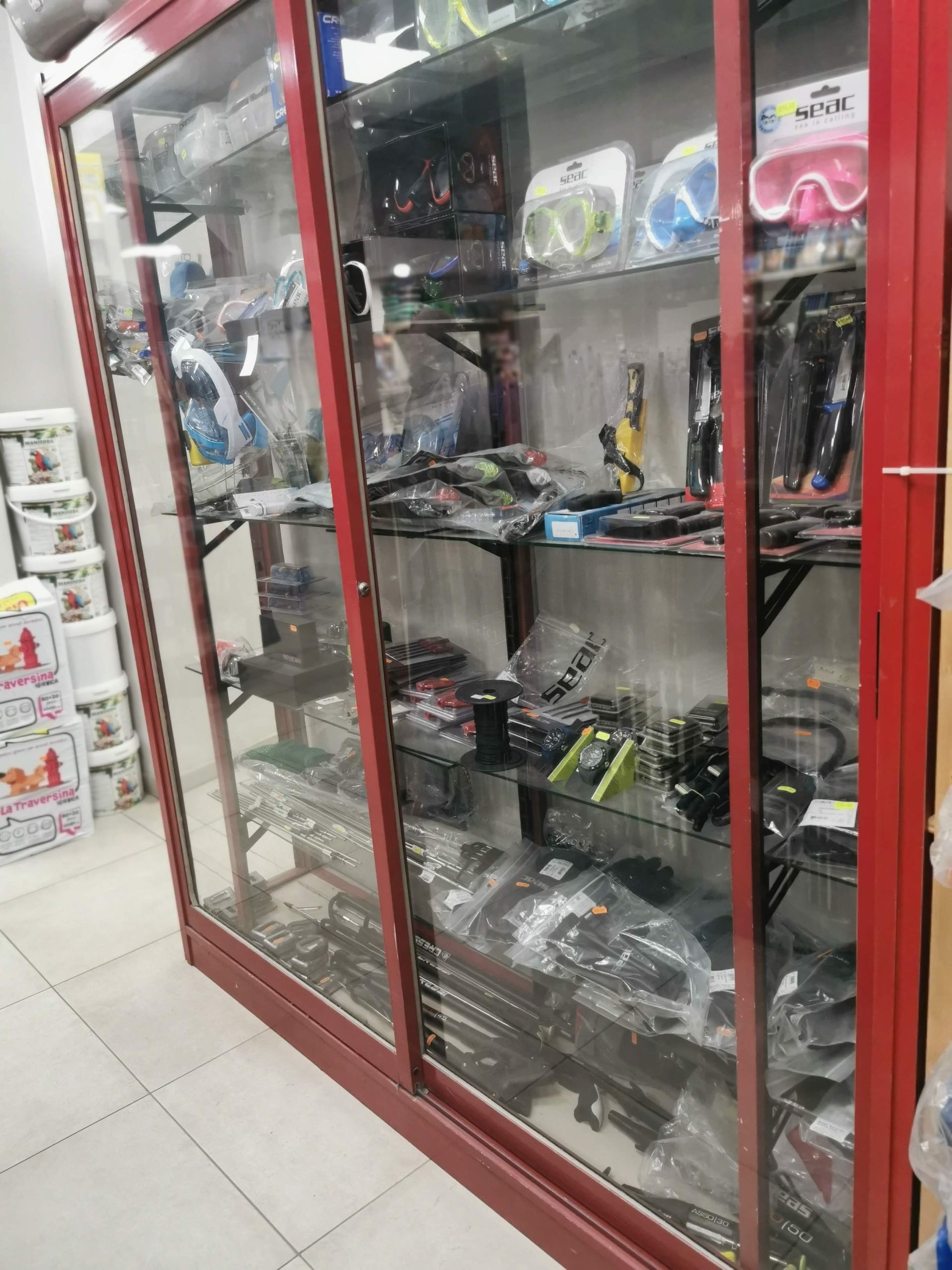 All'interno di un negozio, una vetrina con cornice rossa espone diverse maschere da nuoto e attrezzatura per lo snorkeling su degli scaffali.