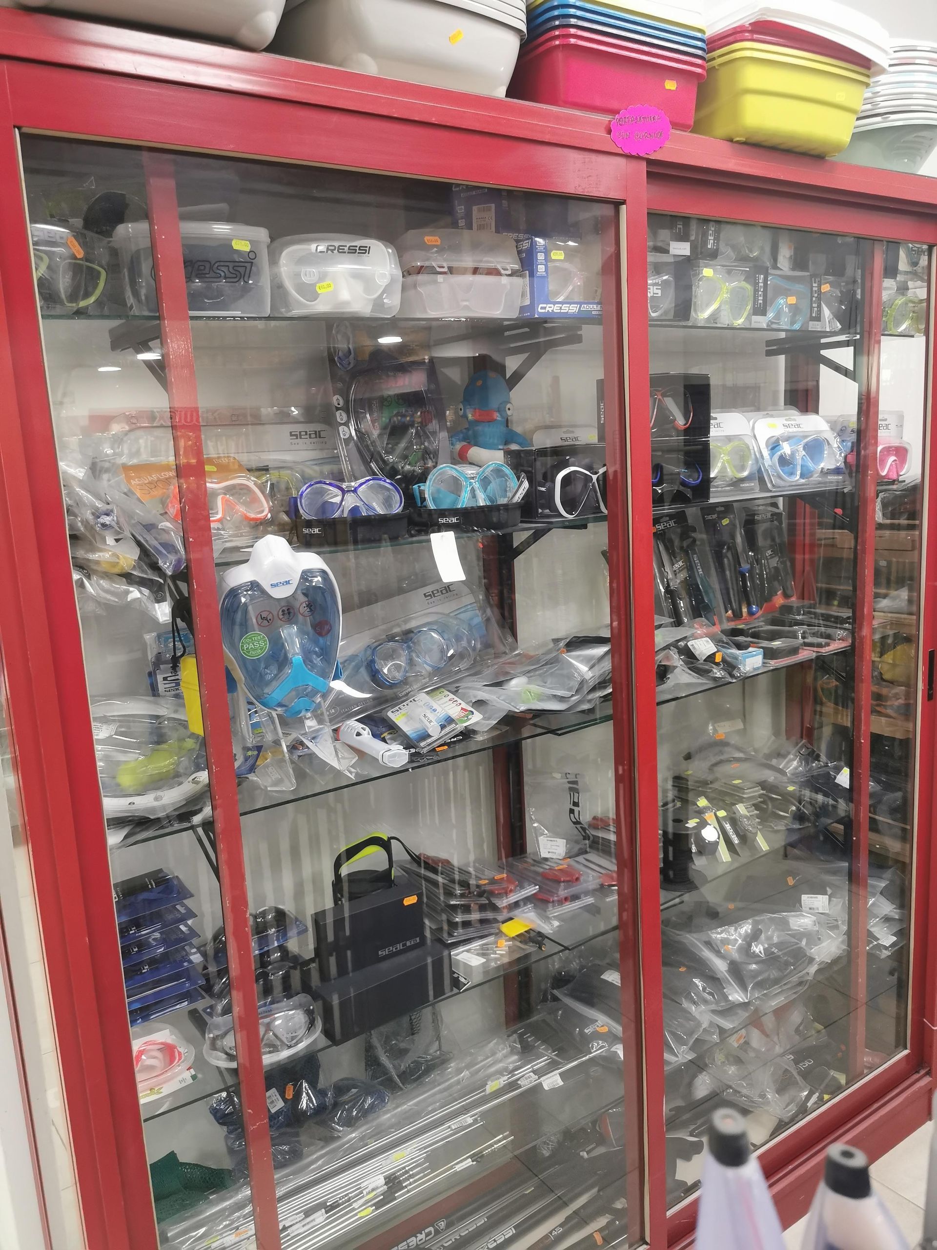 Una vetrina rossa piena di maschere da snorkeling, occhialini e attrezzatura subacquea di vario tipo, con contenitori per riporre gli oggetti sulla parte superiore.