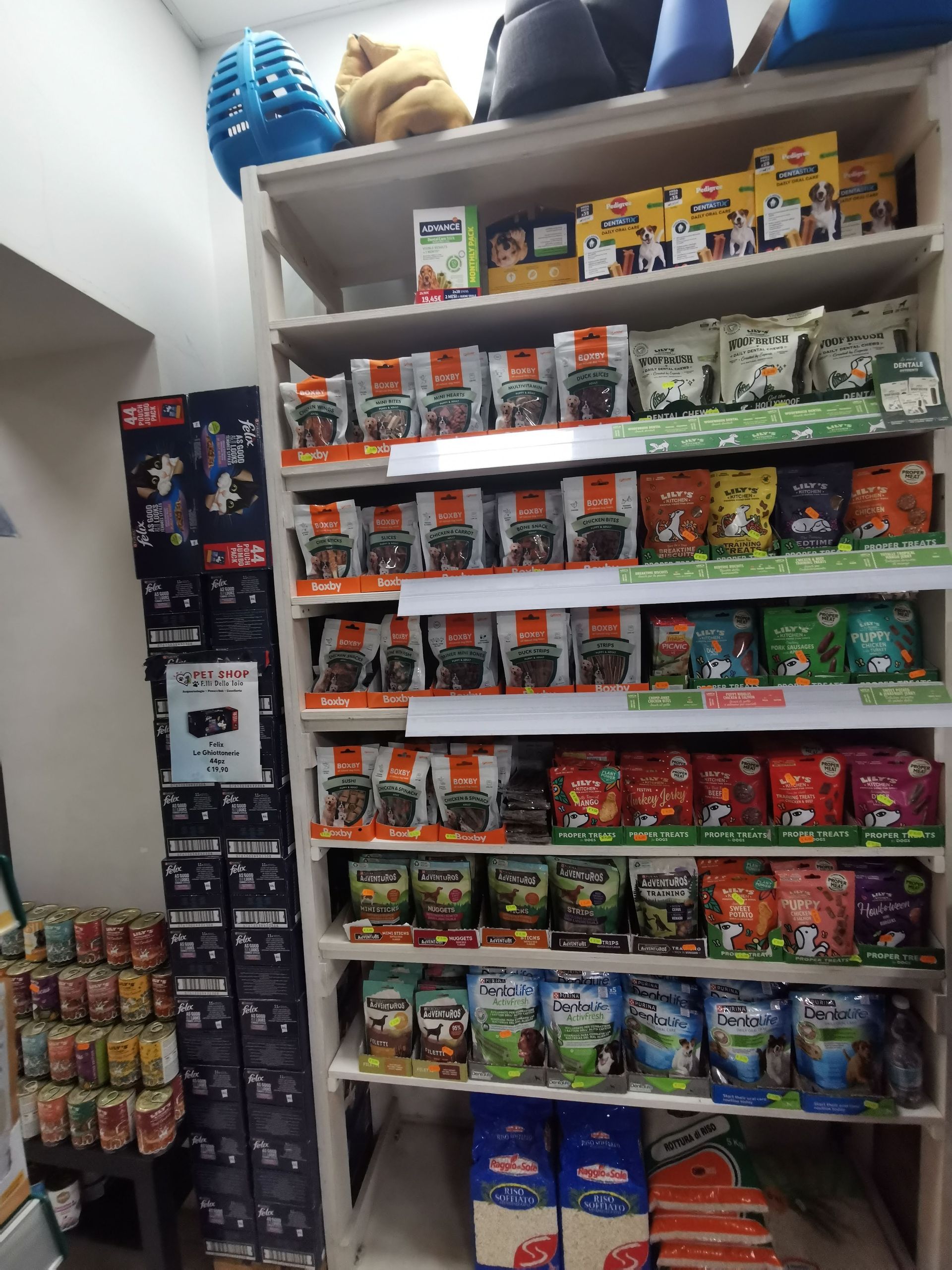 Scaffali pieni di vari sacchetti e contenitori di cibo per animali confezionati, disposti per marca e tipologia, in un ambiente di negozio al dettaglio.