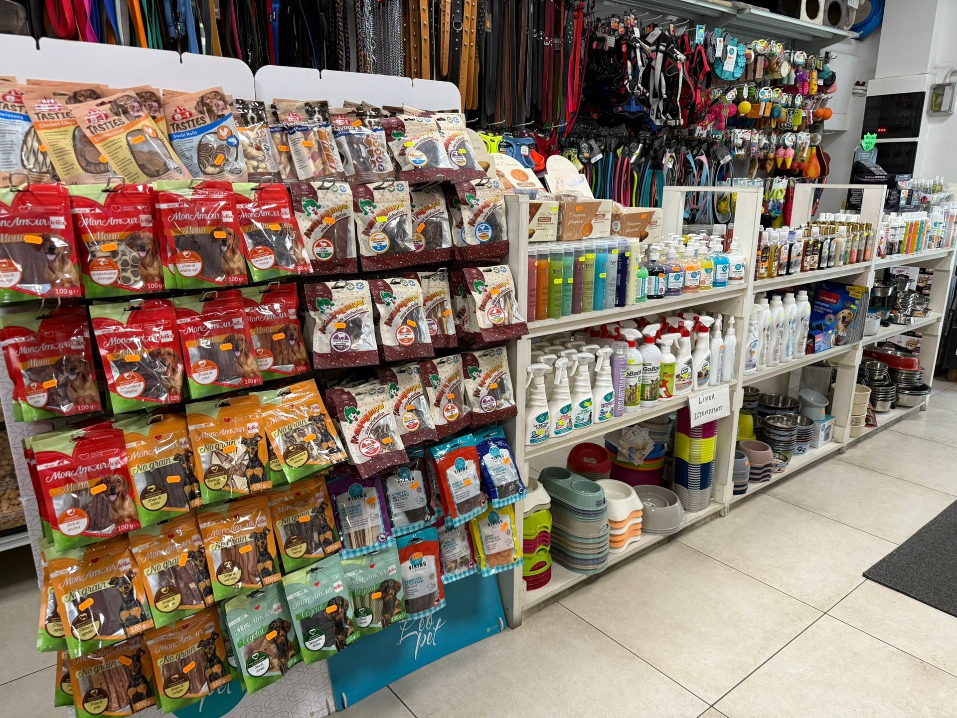 Corridoio di un negozio di articoli per animali con scaffali pieni di snack confezionati, spray detergenti e accessori per animali domestici.