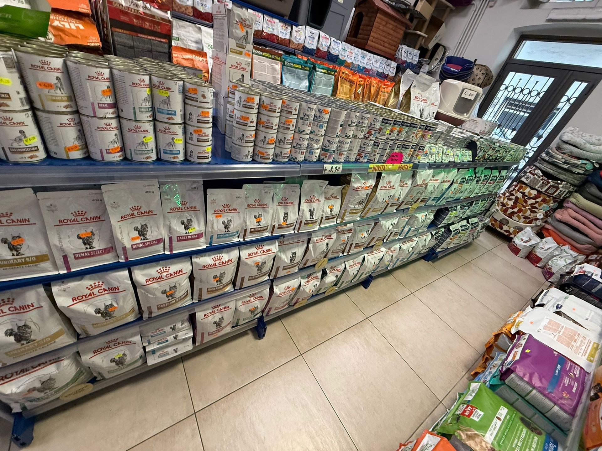 Uno scaffale di un negozio di animali pieno di lattine e sacchetti di cibo per animali, disposti ordinatamente in file.