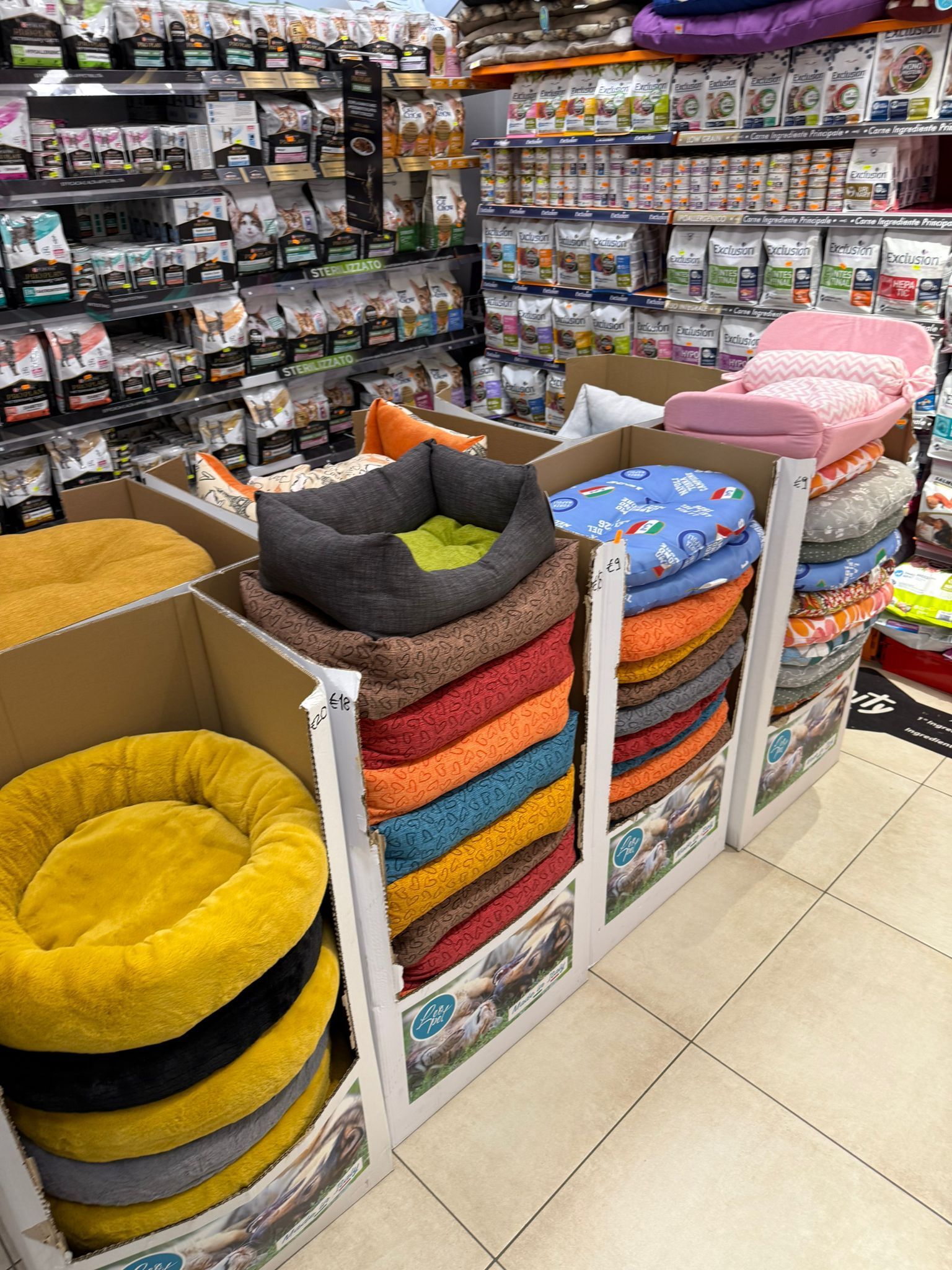 Un'esposizione in negozio che mostra diverse cucce per animali domestici, colorate, rotonde e rettangolari, impilate in contenitori di cartone.
