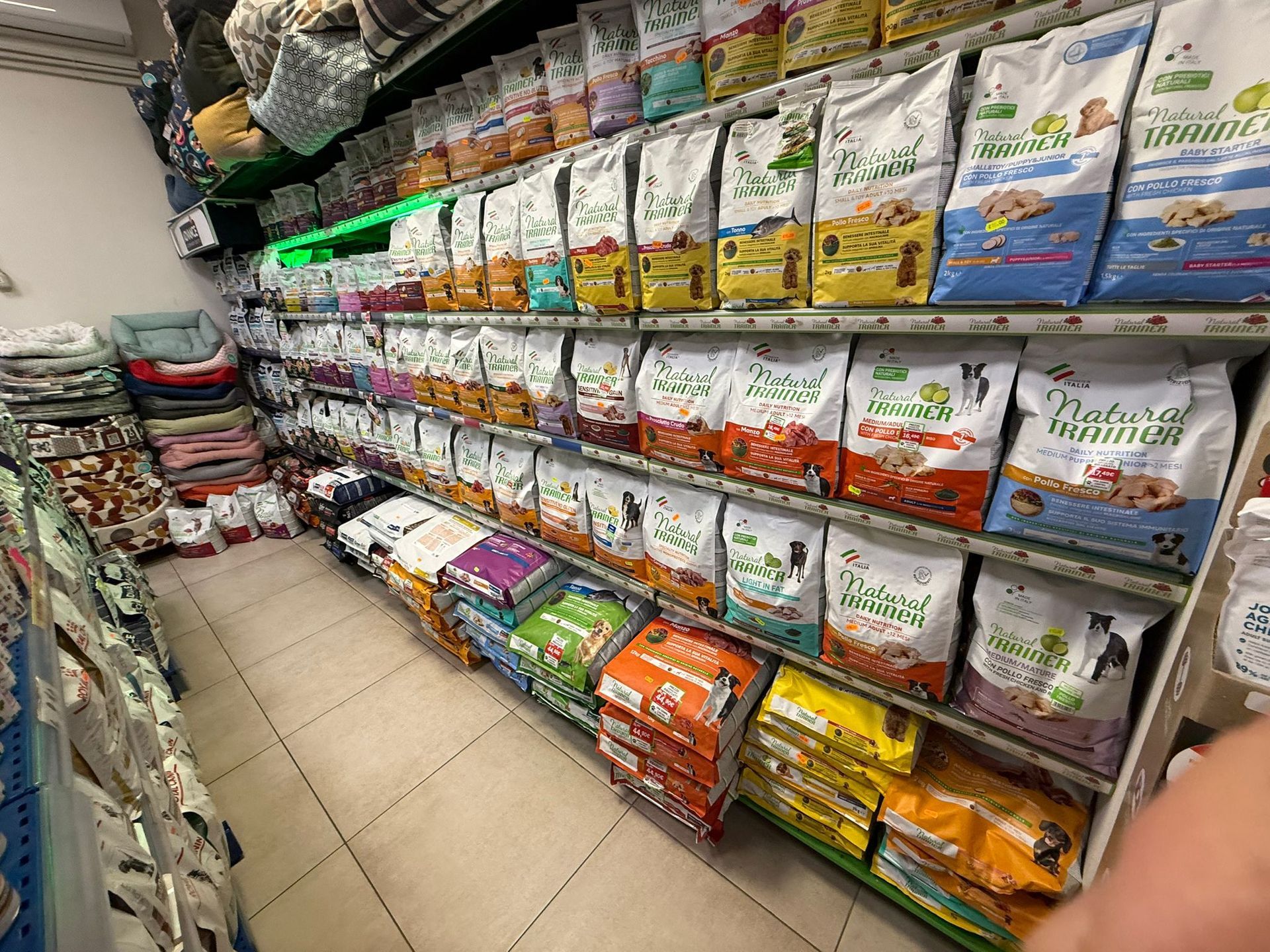 Il corridoio di un negozio di animali domestici mostra scaffali pieni di sacchi di cibo per cani e gatti in confezioni colorate.