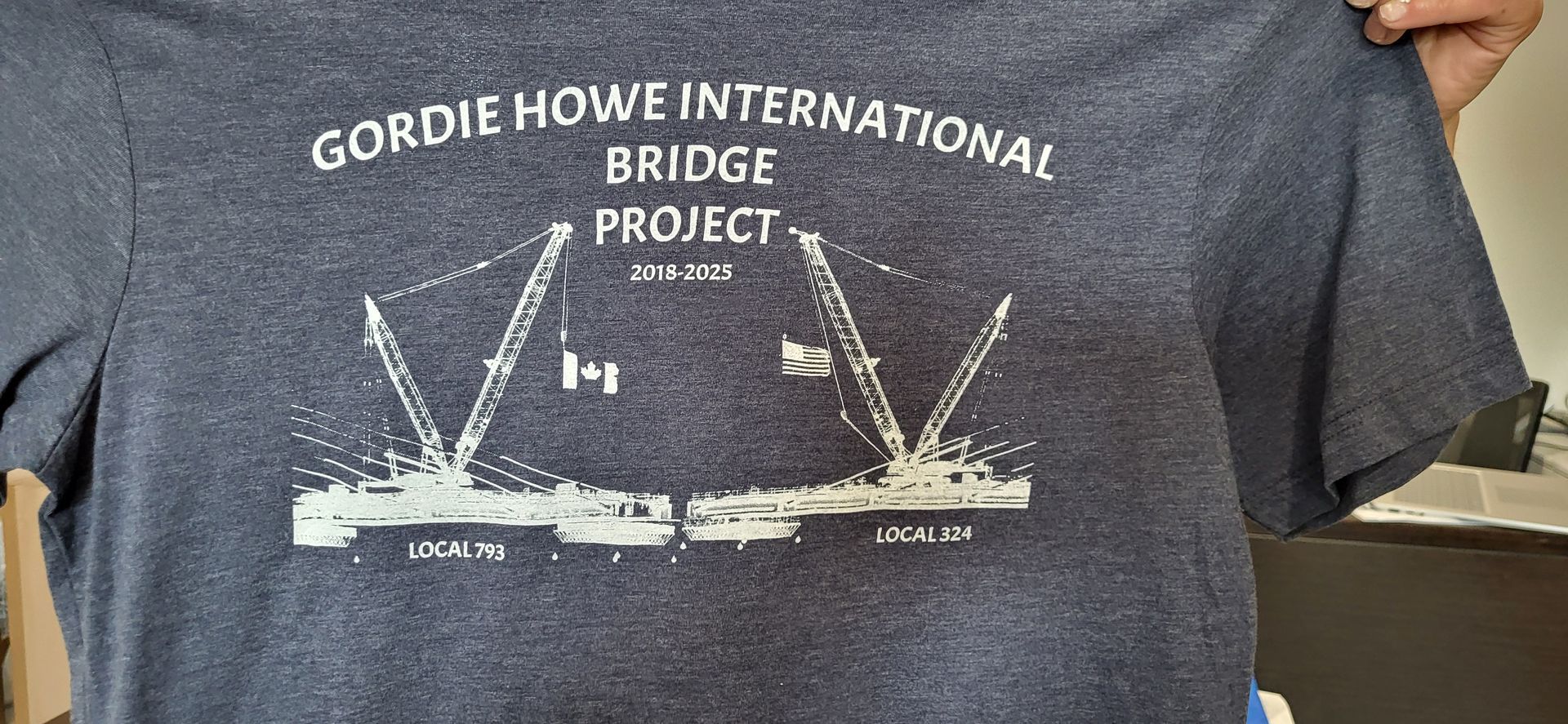 Dark blue t-shirt with a white graphic for the Gordie Howe International Bridge Project. Shows a bridge and cranes.
