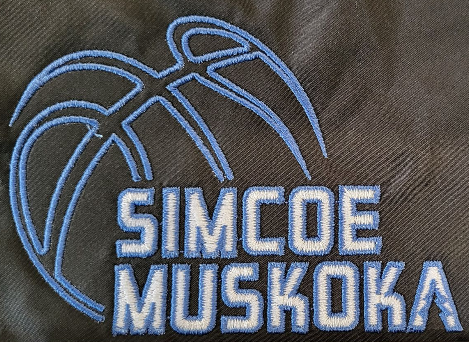 Embroidered logo on dark fabric: light blue basketball and text 