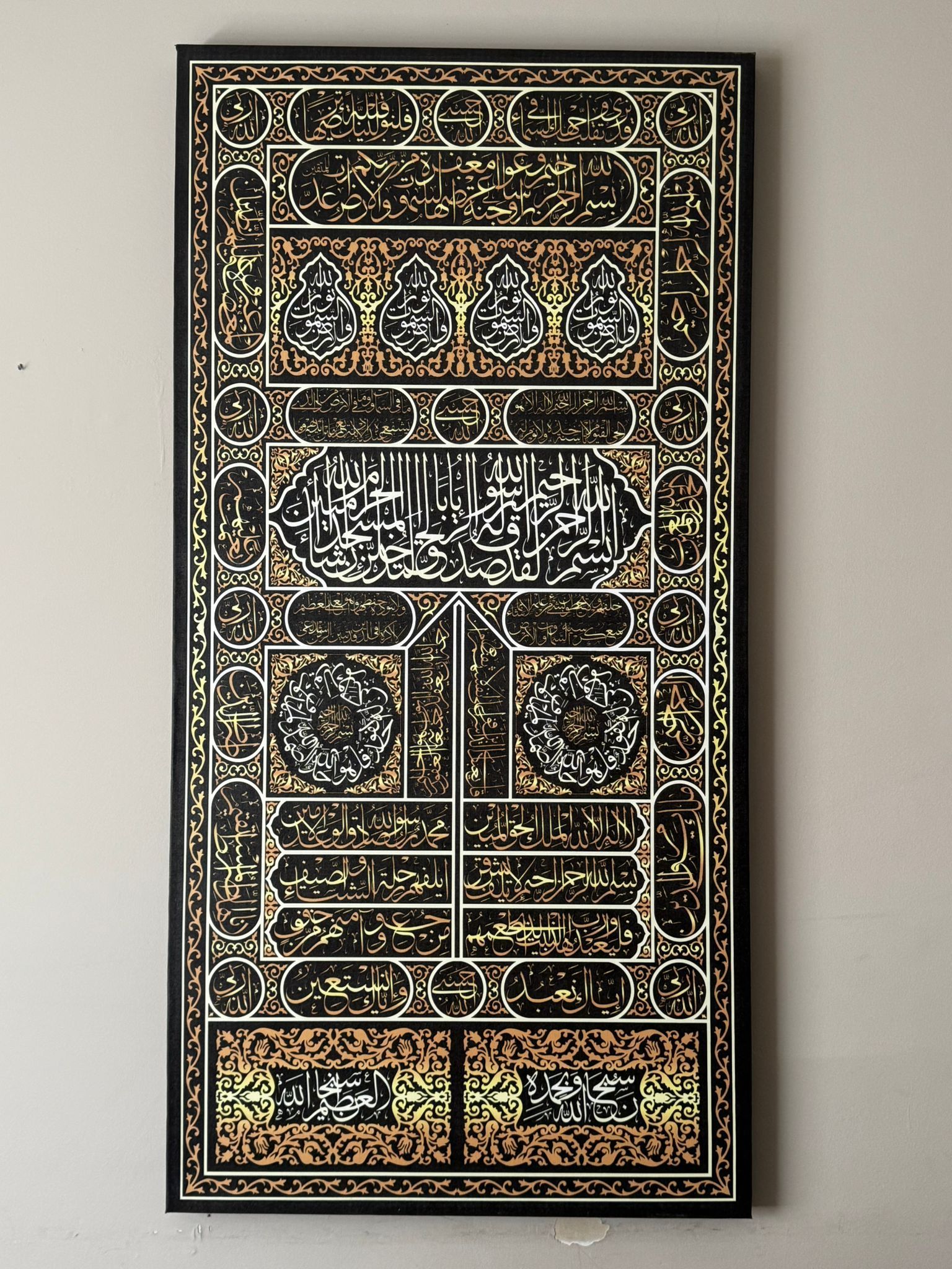 Islamic calligraphy art, gold and black rectangular panel. Arabic script and geometric design on a black background.