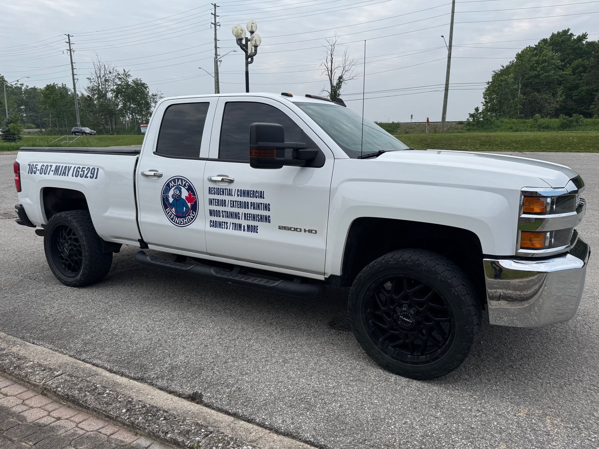 White pickup truck with black wheels, parked on a gray surface; business logo on the side.