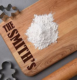 Wooden cutting board with flour, gingerbread men cutters, and a rolling pin.