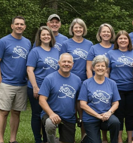 Group of people wearing blue shirts with a white design; standing outside near trees.