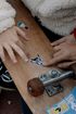 Hands pointing at stickers on a wooden skateboard, with rusty wheels.