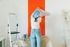Woman wallpapering an orange polka dot wall with a ladder and supplies nearby.
