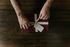 Hands tying a white ribbon around a burgundy gift box on a dark wooden table.