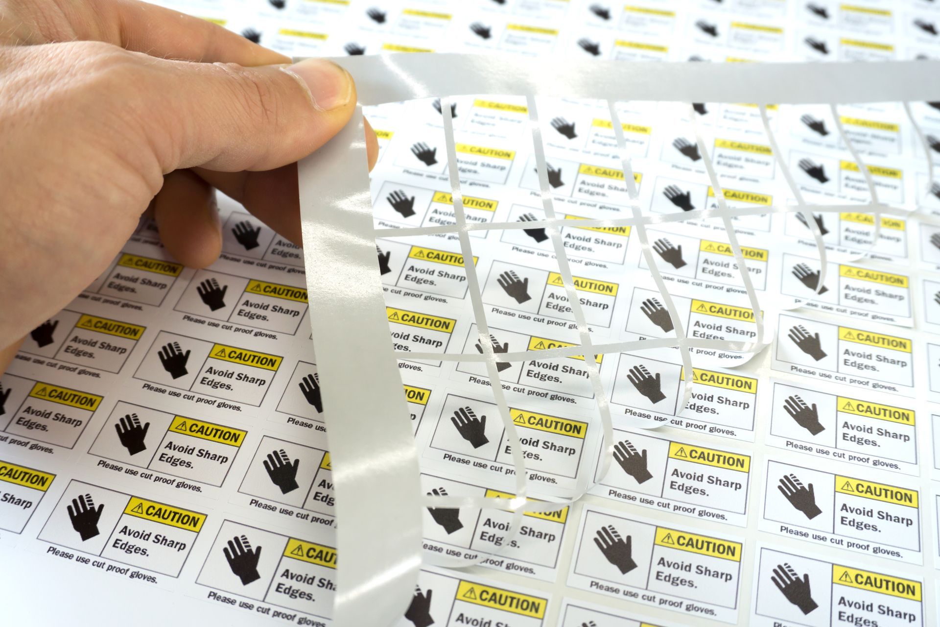 Hand peeling a sheet of printed labels with black gloves and text on a white background.