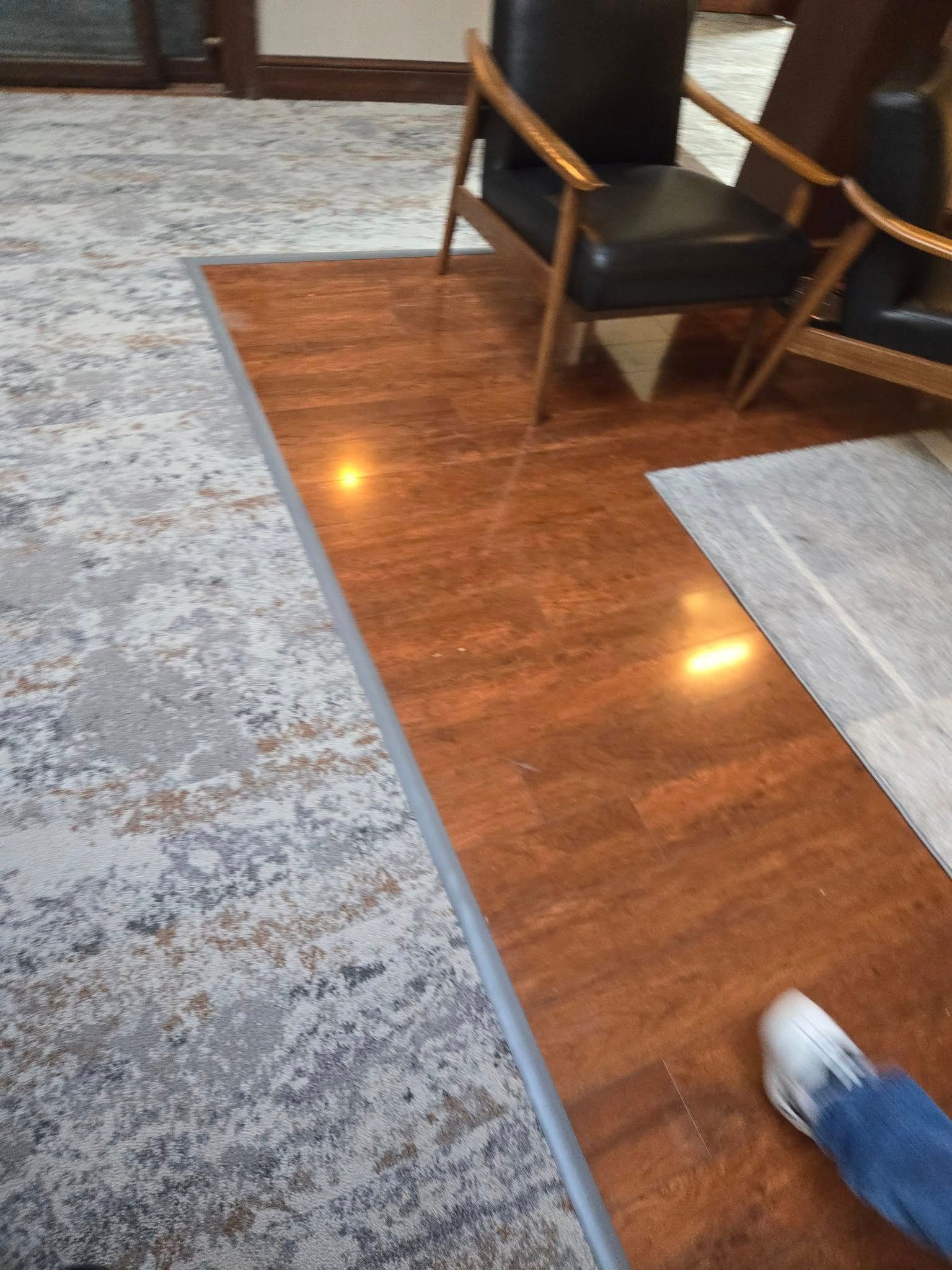 A person is standing on a wooden floor in a room with chairs and a rug.