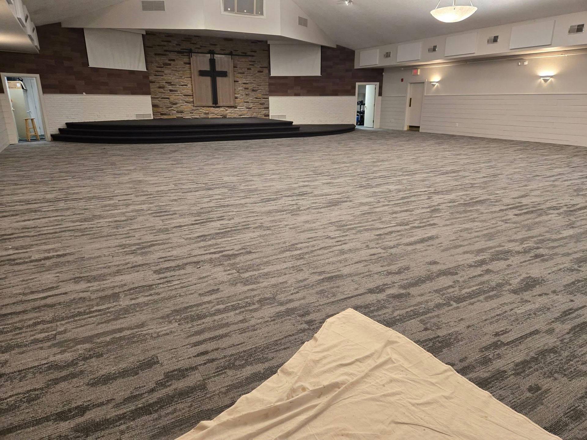 A large empty room with a carpeted floor and a cross on the wall.