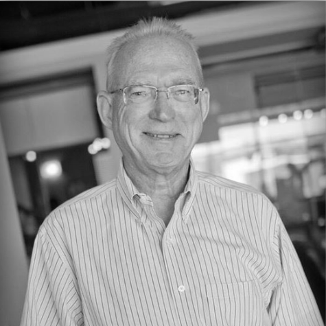 A man wearing glasses and a striped shirt is smiling in a black and white photo.