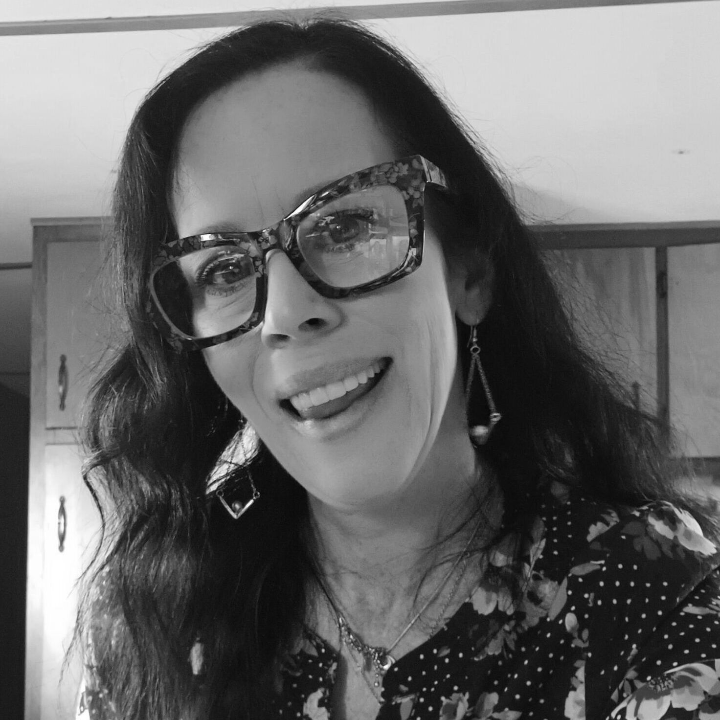 A woman wearing glasses and earrings is smiling in a black and white photo.