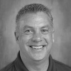 A man wearing glasses and a striped shirt is smiling in a black and white photo.