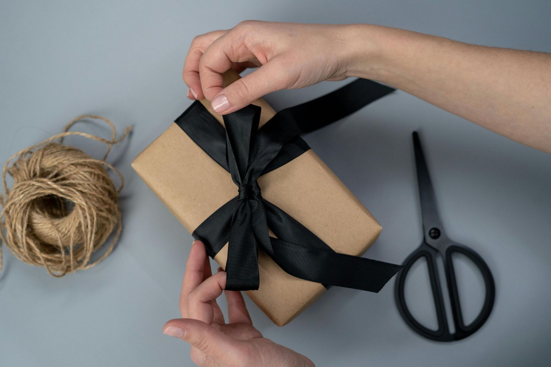 A person is wrapping a gift with a black ribbon and scissors.