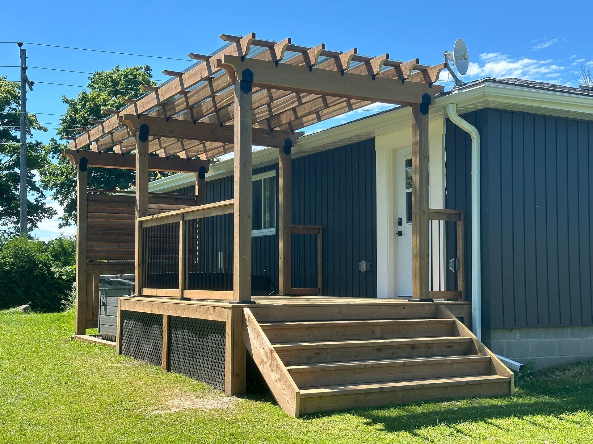 A wooden deck with stairs and a pergola in front of a house.