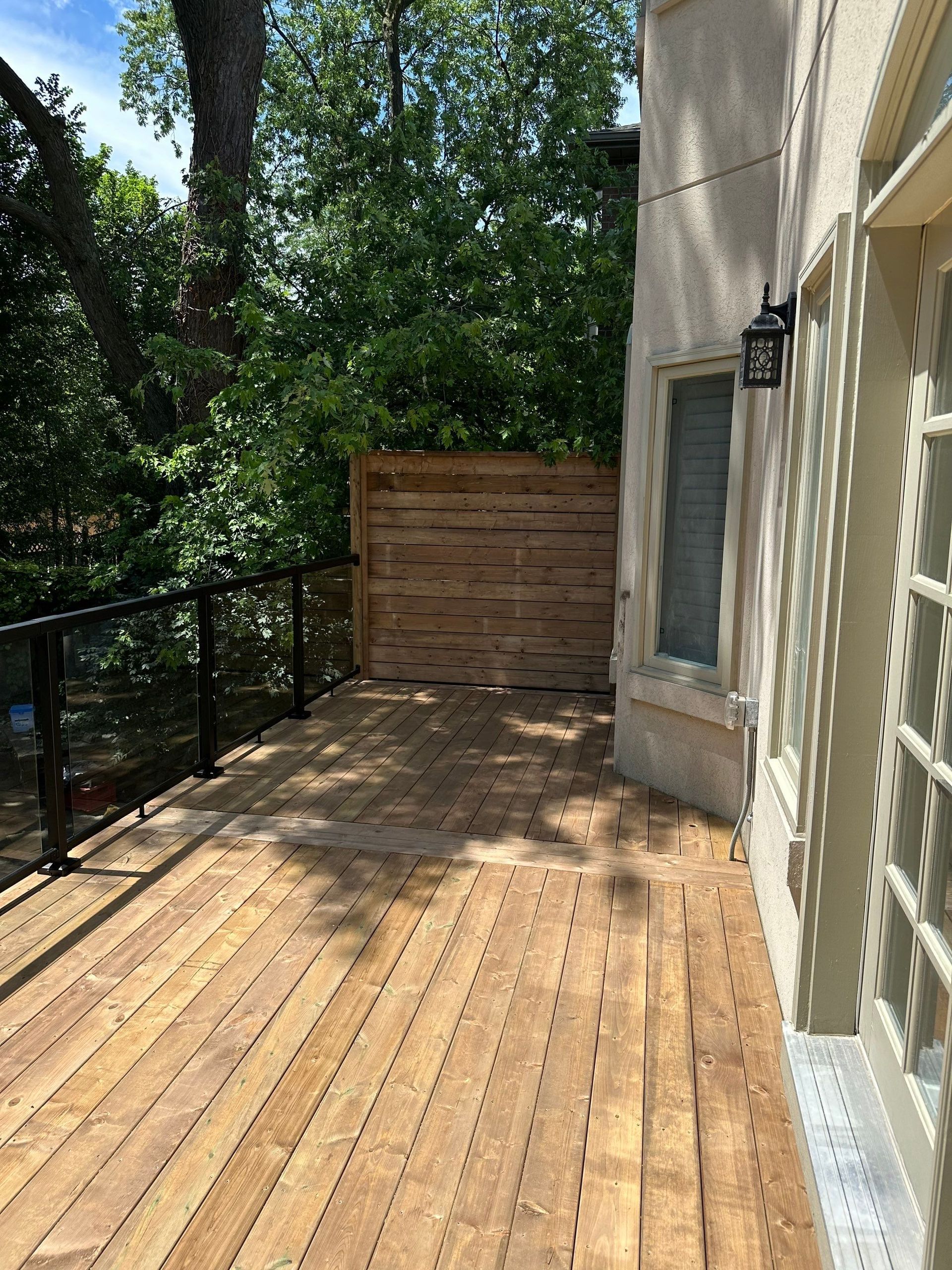 A wooden deck with a glass railing and a fence in the backyard of a house.
