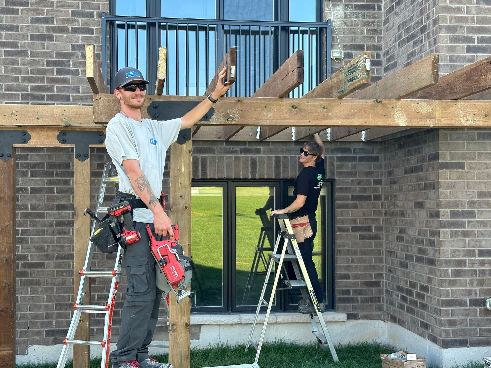 Two men are working on a wooden structure in front of a brick building.