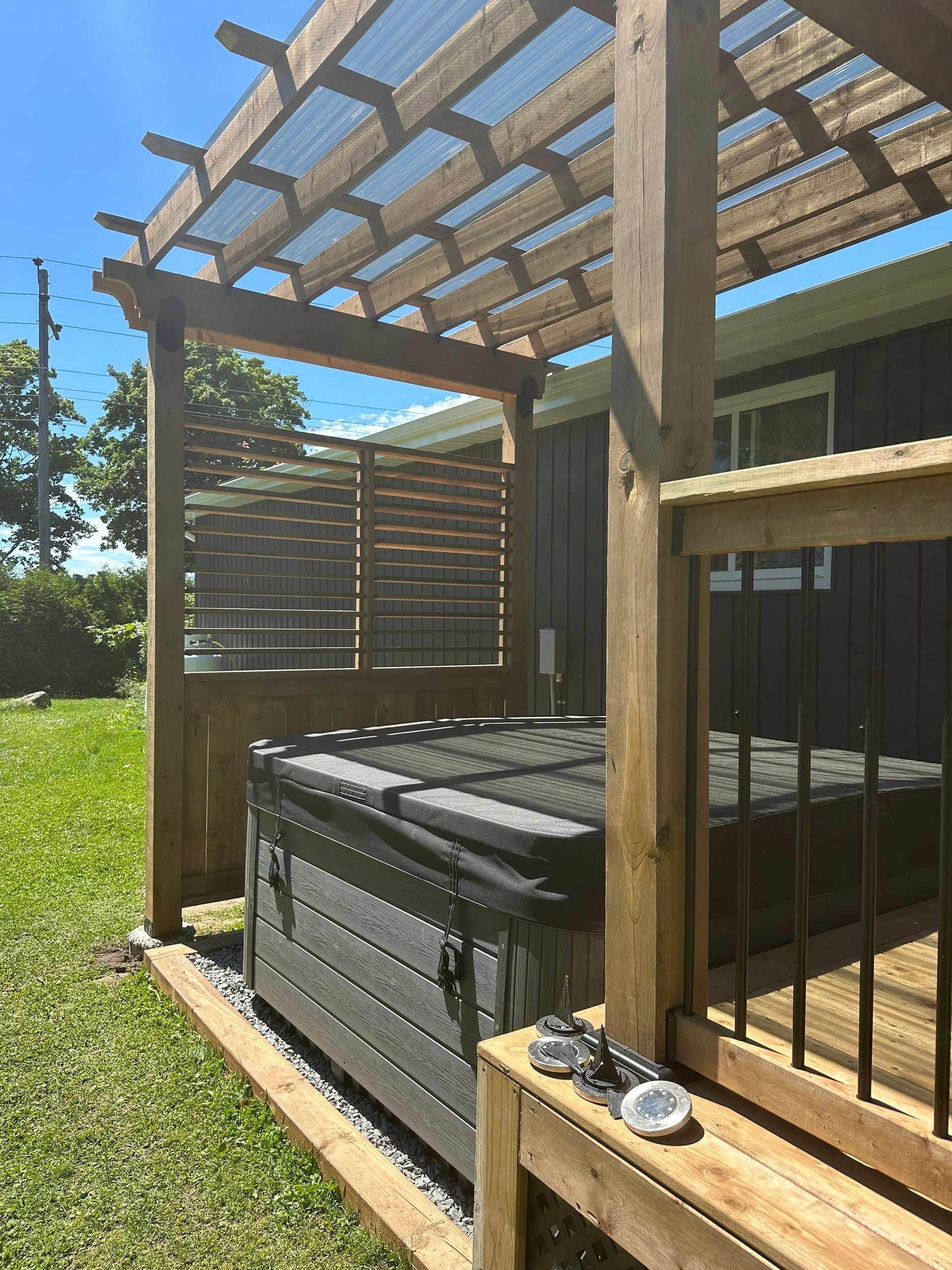 A hot tub is under a wooden pergola in a backyard.