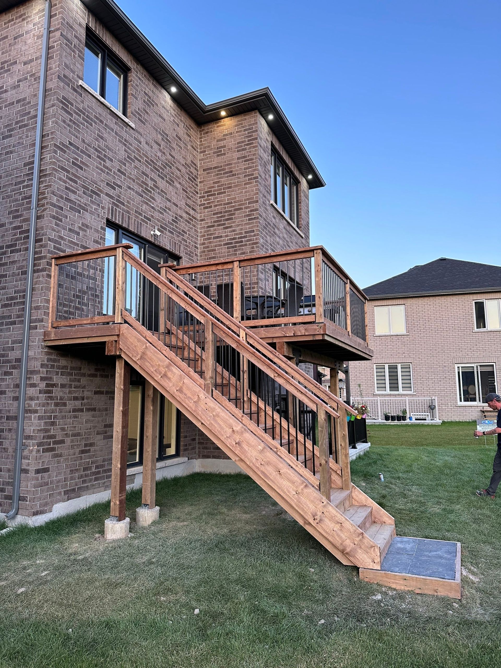 A wooden deck with stairs leading up to it is in front of a brick house.