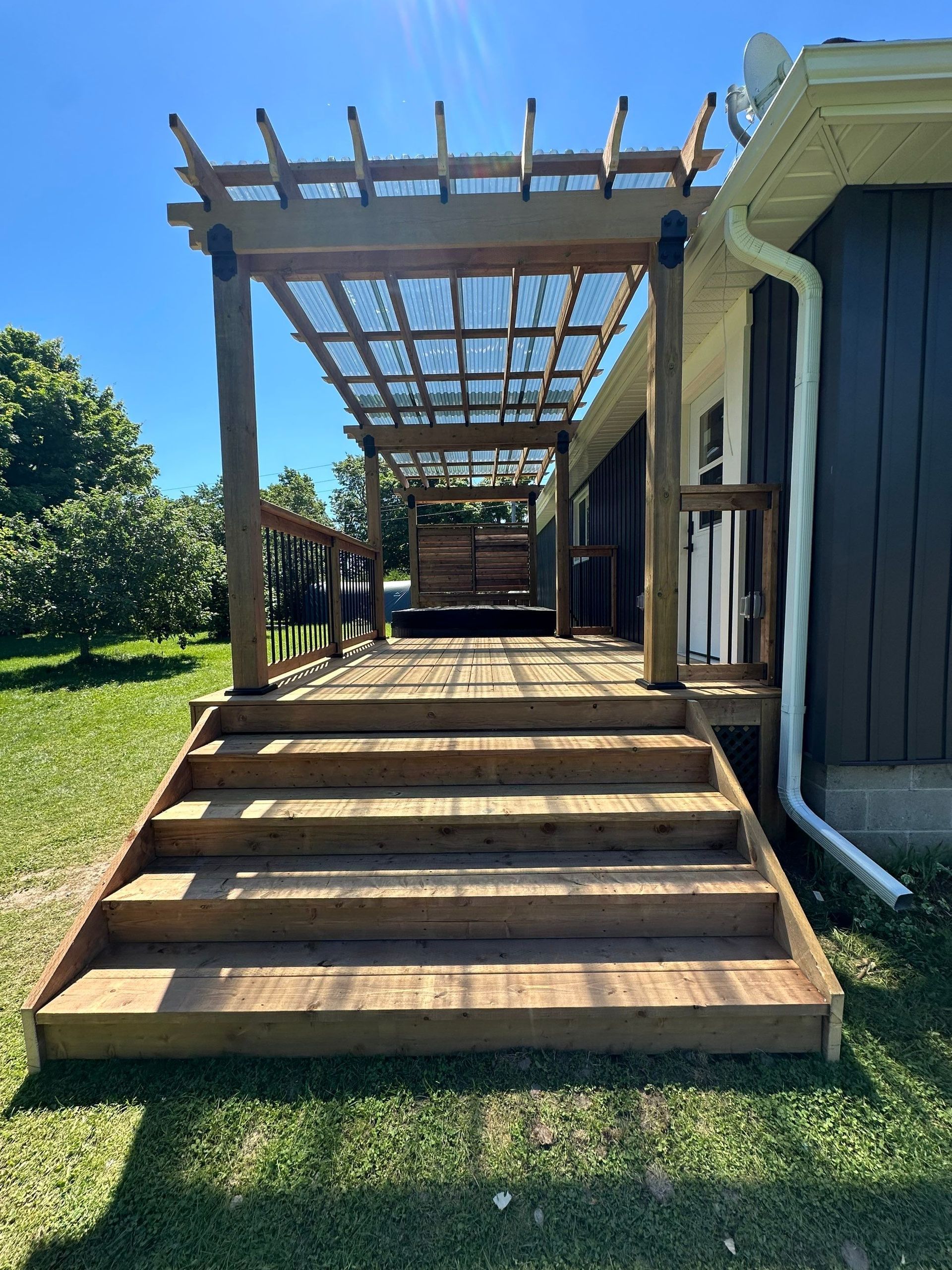 A wooden deck with stairs and a pergola in front of a house.