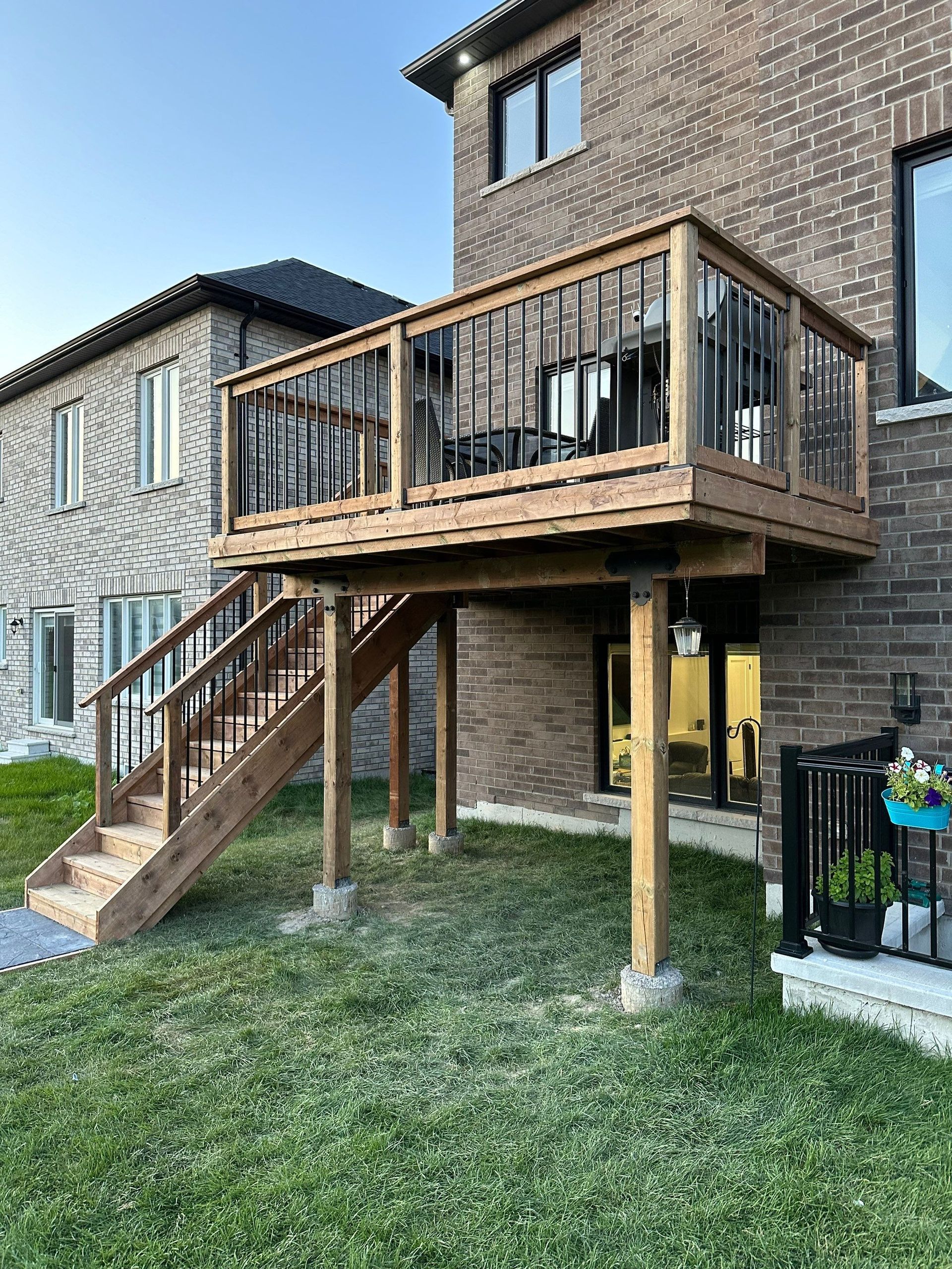 A wooden deck with stairs is in the backyard of a brick house.