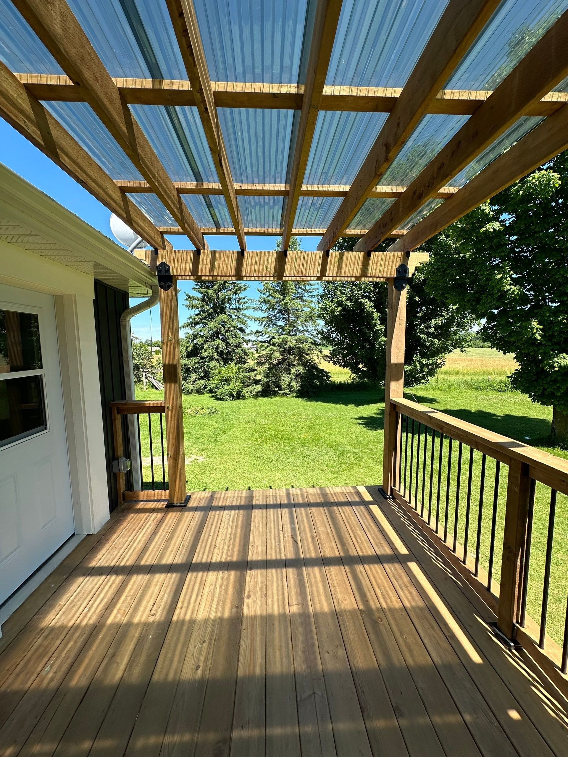 A wooden deck with a clear plastic roof and a pergola.